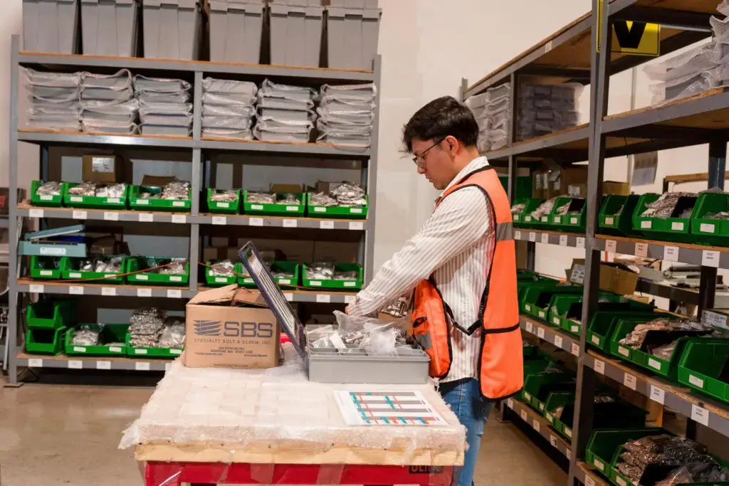 Employee preparing organized fastener kits in a warehouse with labeled bins.